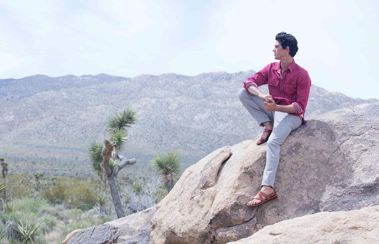 a male model sitting on a rock wearing Jerusalem sandals looking to distance